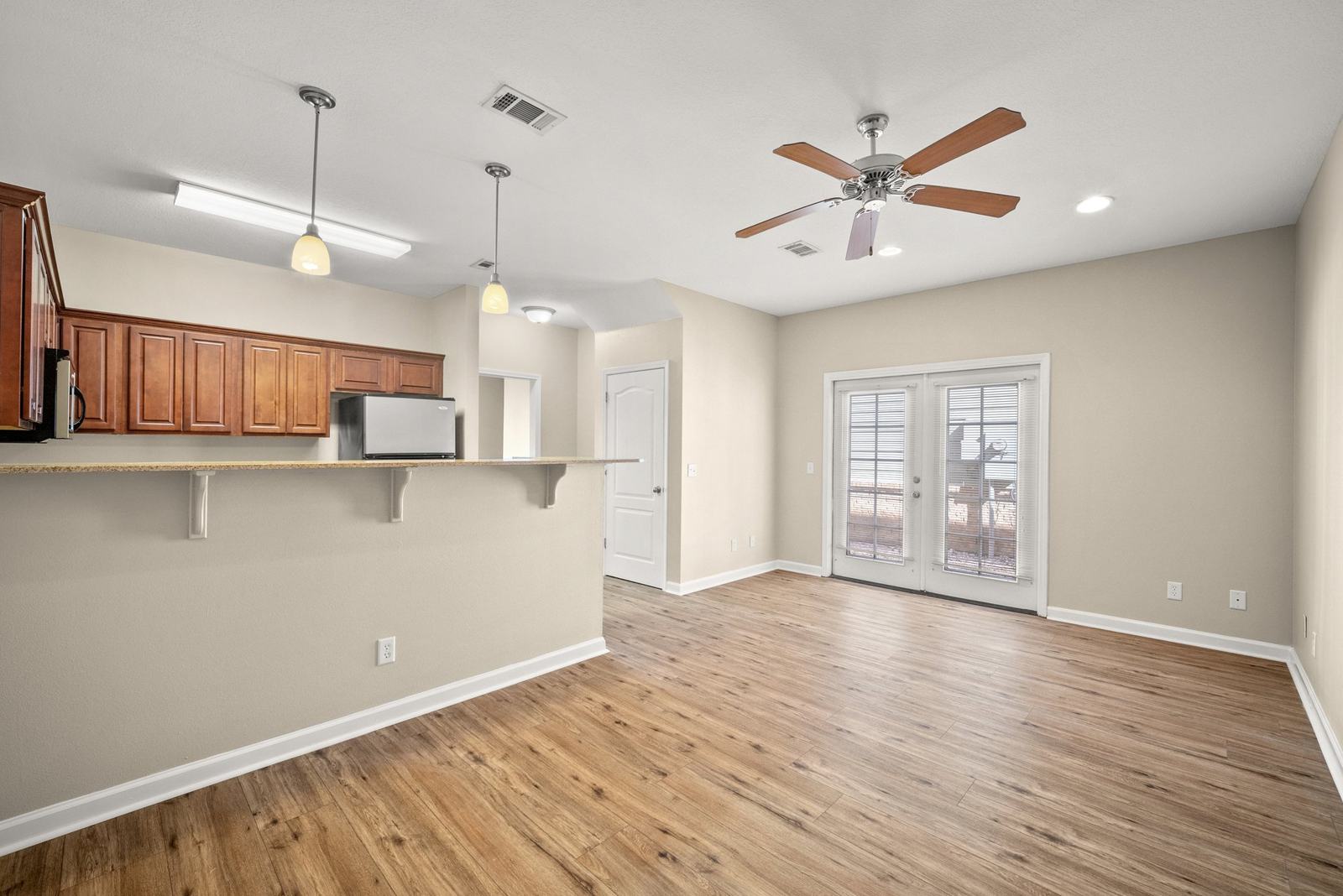 Open living room with wood-look floors, ceiling fan and French doors to the patio